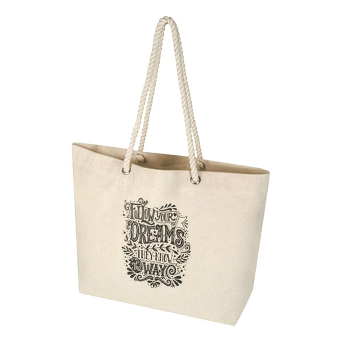 A cream beach tote bag with rope handles and a decorative design. It features a logo on one side.