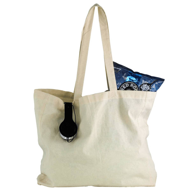 A natural cotton shopper tote in cream, featuring a black headphone and a bag of snacks inside.