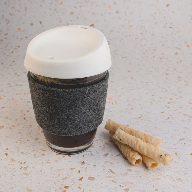 A reusable coffee cup in grey with a white silicone lid and RPET band, accompanied by rolled wafers.