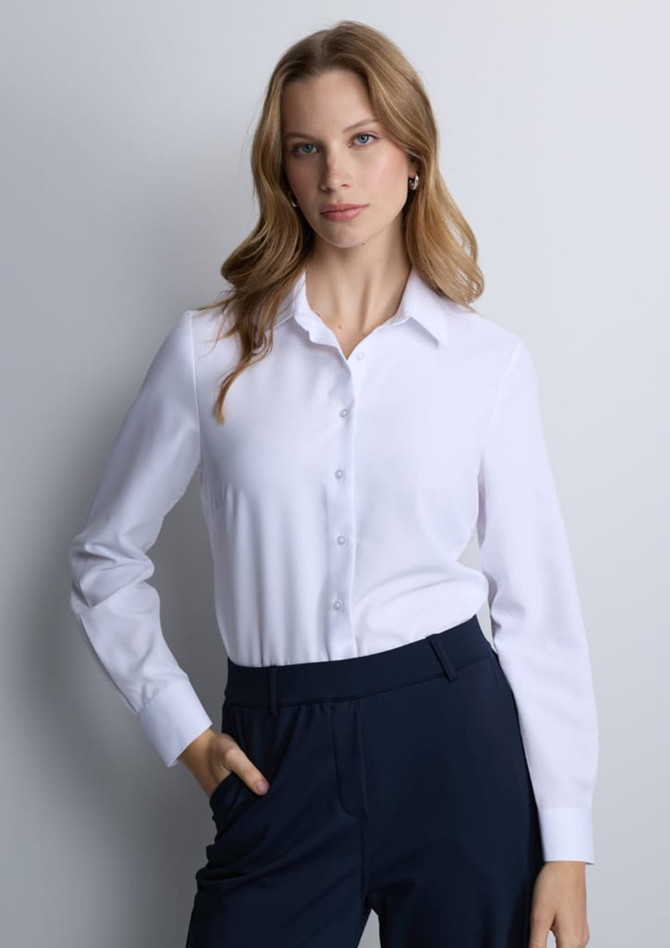A women's long sleeve shirt in white with a button-up front and a collar, paired with dark pants.