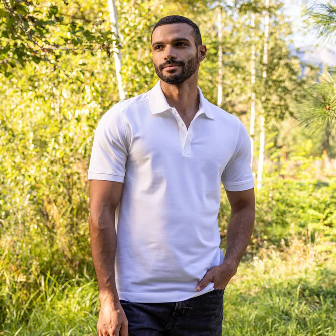 A men's polo shirt in white, featuring a collar and short sleeves, displayed in a natural outdoor setting.