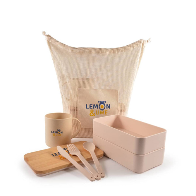A beige mesh bag with a logo, containing a mug, two food containers, a bamboo tray, and cutlery in soft pink.