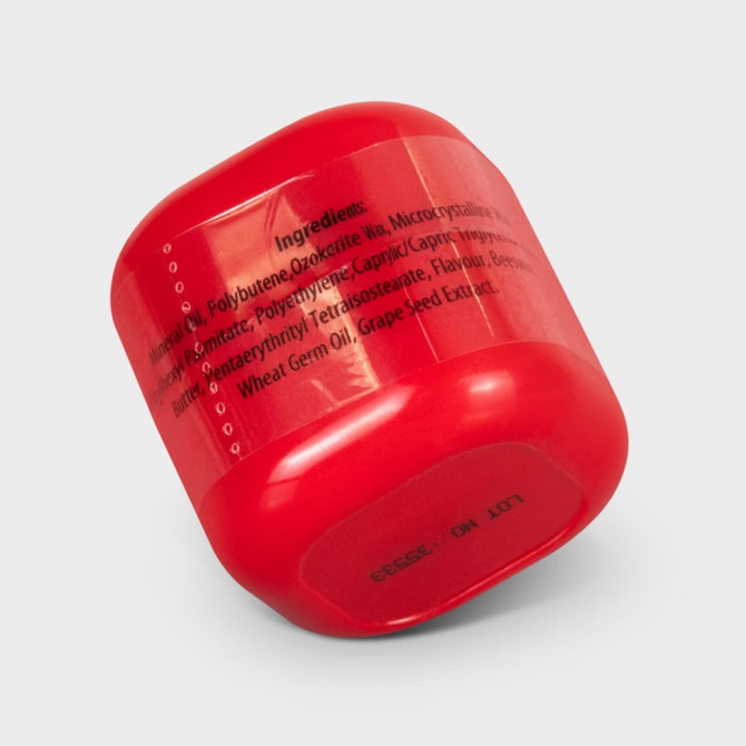 A red lip balm container with a rounded shape, featuring a logo and ingredients listed on the side.