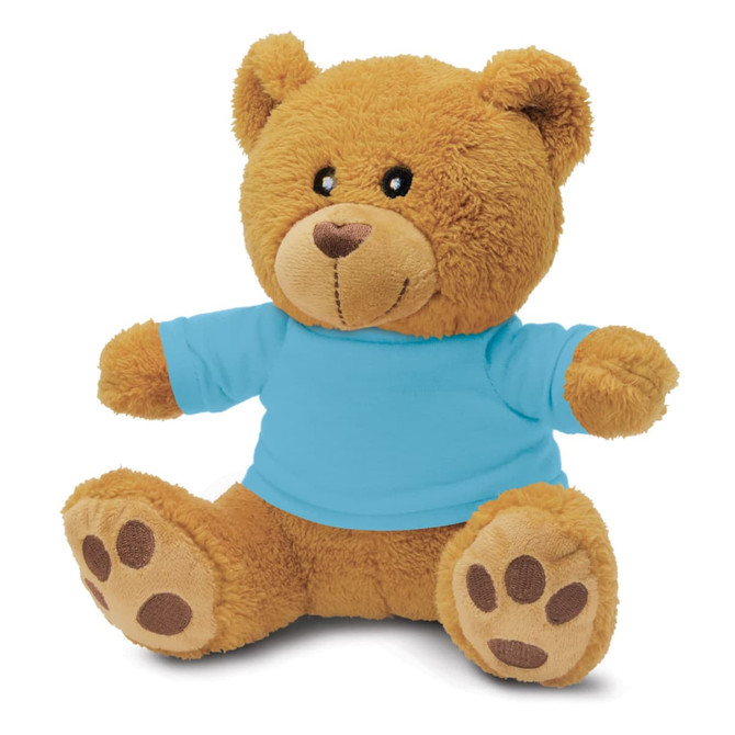 A plush teddy bear toy in tan, wearing a blue T-shirt, with brown paw accents and round, friendly features.