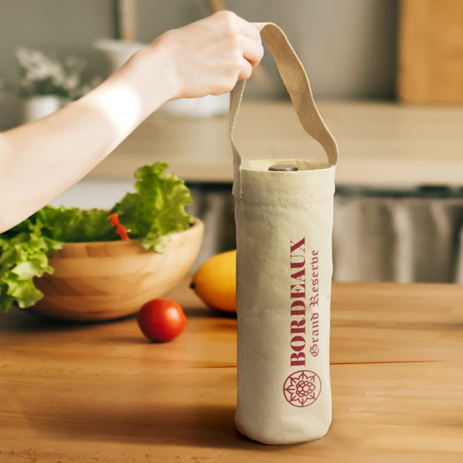 A cotton wine tote bag in natural colour with a logo, held by a hand. There are vegetables and fruits in the background.