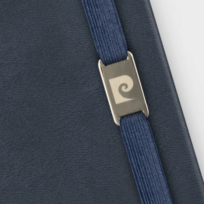 A navy ribbon closure adorns a dark leather notebook with a branded metal accent.
