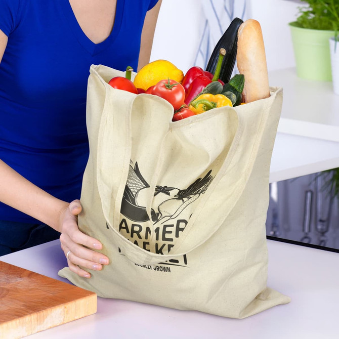 A beige tote bag filled with fresh vegetables and a baguette, featuring a logo on the front.