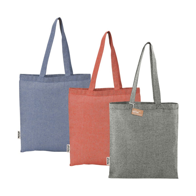 Three recycled cotton twill tote bags in blue, red, and grey, each featuring a handle and a logo label.