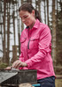 A long sleeve women's button-up shirt in pink, featuring chest pockets, worn outdoors among trees.