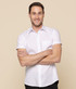 A short-sleeved, white button-up shirt worn by a smiling male model with crossed arms against a neutral background.