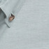 A close-up of a light grey work shirt with a button and textured fabric. The shirt features a logo.