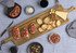 A wooden tapas serving board features bruschetta, crackers, cheese, olives, and drinks on a textured blue tablecloth.