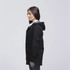 A black twill jacket with a hood, featuring a side view of a woman wearing it. The jacket has a logo. A black twill jacket with a hood, featuring a side view of a woman wearing it. The jacket has a logo.