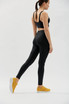 Black active leggings worn by a model, paired with a black sports top and yellow trainers, featuring a logo.