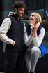 A black softshell vest is worn by a man, while a woman smiles in a blue softshell vest, both against a modern backdrop.
