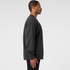 A dark grey jumper featuring a simple design, displayed on a model from the side. The jumper has a logo on it.