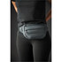 A quilted waist bag in dark green worn around the waist by a person in black activewear. It features a logo.