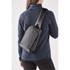 A grey and black sling backpack worn over the shoulder, displayed on a person in a blue jacket.