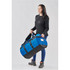 A woman holds a large blue and black duffle bag with straps. The bag features a logo.