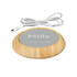 A USB cup warmer with a wooden base and a smooth grey surface, featuring a brand logo. It has a white power cable.