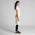 A linen apron in natural beige, featuring a side tie and a logo, worn over a white shirt and black trousers.