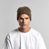 A beanie in a muted brown colour, worn by a model, featuring ribbed texture and a logo.