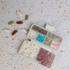 A compact white pill organizer with multiple compartments filled with various colored pills scattered around.