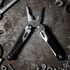 A black and silver multi-tool with pliers and various tools, surrounded by metal tools and screws. It features a logo.