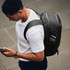 A black backpack is worn by a person looking at their phone, with a drink bottle visible in a side pocket.