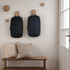 Two dark blue backpacks hang on a wall, alongside wooden hooks, with a bench and cushions in the foreground.