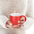 A coffee mug in vibrant red with a white interior held in hands, set against a soft, knitted sweater.