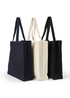 Three heavy tote bags in navy, cream, and black, each featuring long handles and a logo.