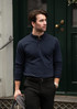 A navy blue polo shirt with a collar and button placket, modelled by a man in smart casual attire, holding a jacket.