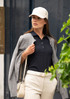 A navy polo shirt paired with a grey cardigan, featuring a white cap and cream trousers. Includes a bag and foliage in the background.