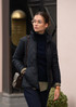 A black quilted women's jacket, styled with a navy top and carrying a handbag, features a sleek design and a logo.
