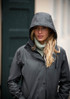 A woman in a black rain jacket with a hood, standing outdoors with her long, wavy hair slightly wet.