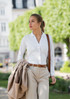 A woman wearing a white polo shirt and striped trousers, carrying a jacket and handbag, walking outdoors.