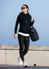 A woman wears a black hoodie and leggings, carrying a bag, walking outdoors against a blue sky.