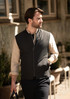 A man wearing a black vest over a light-coloured shirt, walking in an outdoor setting. The vest has a branding logo.