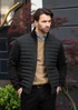A black puffer jacket worn by a man, featuring a zip closure and standing outdoors against a backdrop of greenery.