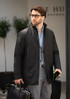 A black men's jacket is worn by a man holding a bag, set in a modern outdoor environment.