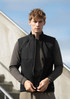 A model wearing a black unisex vest over a long-sleeve brown top, against a stairway and blue sky background.