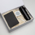 A black notebook, a white speaker, a black drink bottle, and a pen in a gift box with shredded paper.