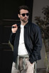 A unisex jacket in navy blue, worn by a man with sunglasses, styled casually with a light-coloured shirt.