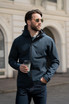 A man wearing a navy blue shell jacket with a hood, holding a coffee cup, and wearing sunglasses.