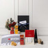 A customised gift set featuring a black box, gourmet treats, a grey towel, and decorative items in red and gold.