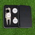 A silver divot tool set with two ball markers, presented in a black box, featuring a logo on the items.