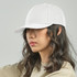 A white cap with a curved brim, featuring an adjustable strap and a logo. The model has wavy hair.
