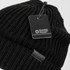 A black knitted beanie with a tag attached and a logo. The beanie features a textured pattern.