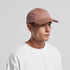 A pink cap with a curved brim and a logo, worn by a model in a white sweatshirt.